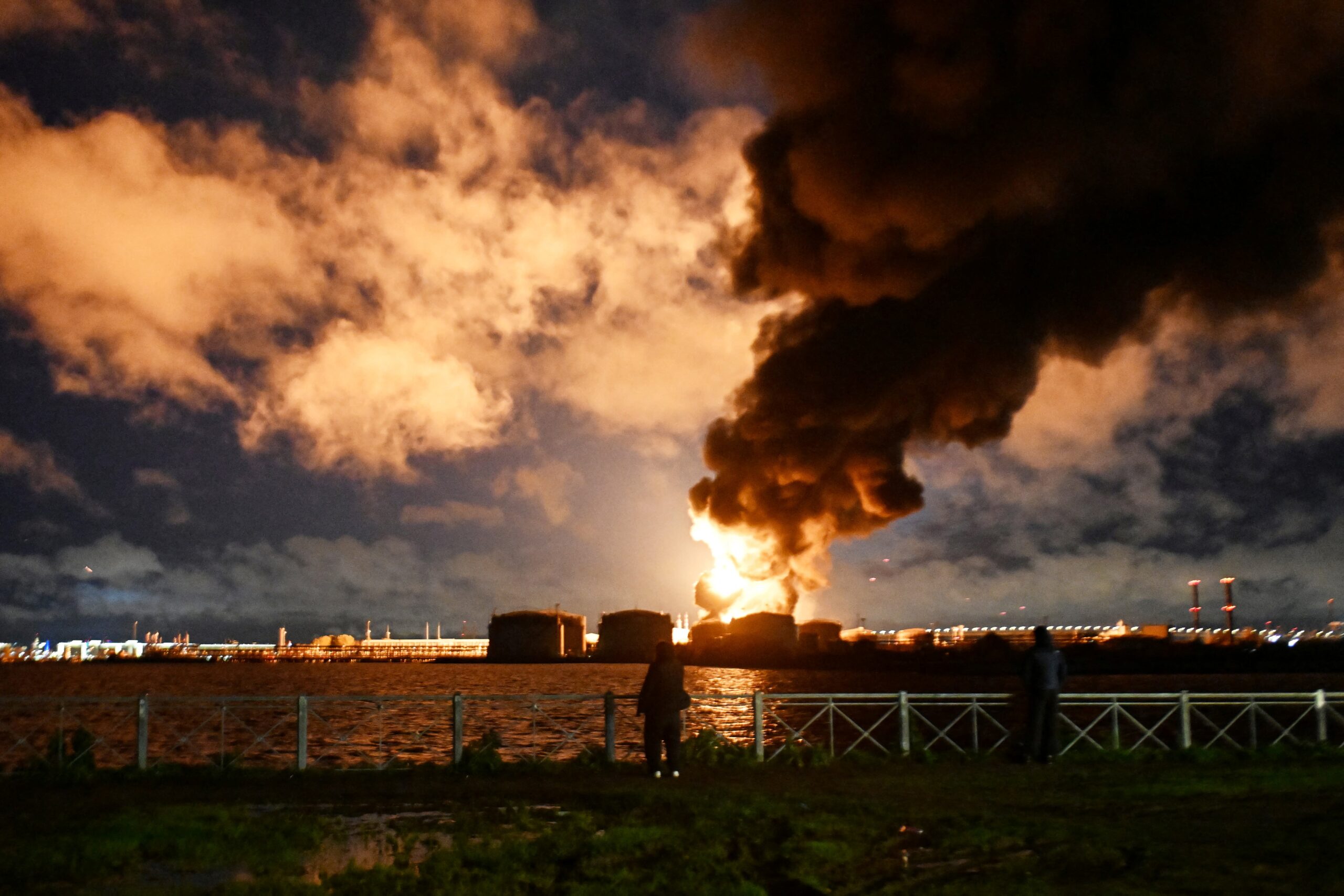 People watch the burning oil terminal following an air attack in Saint Petersburg